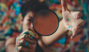 woman with paint on her hands holding magnifying glass
